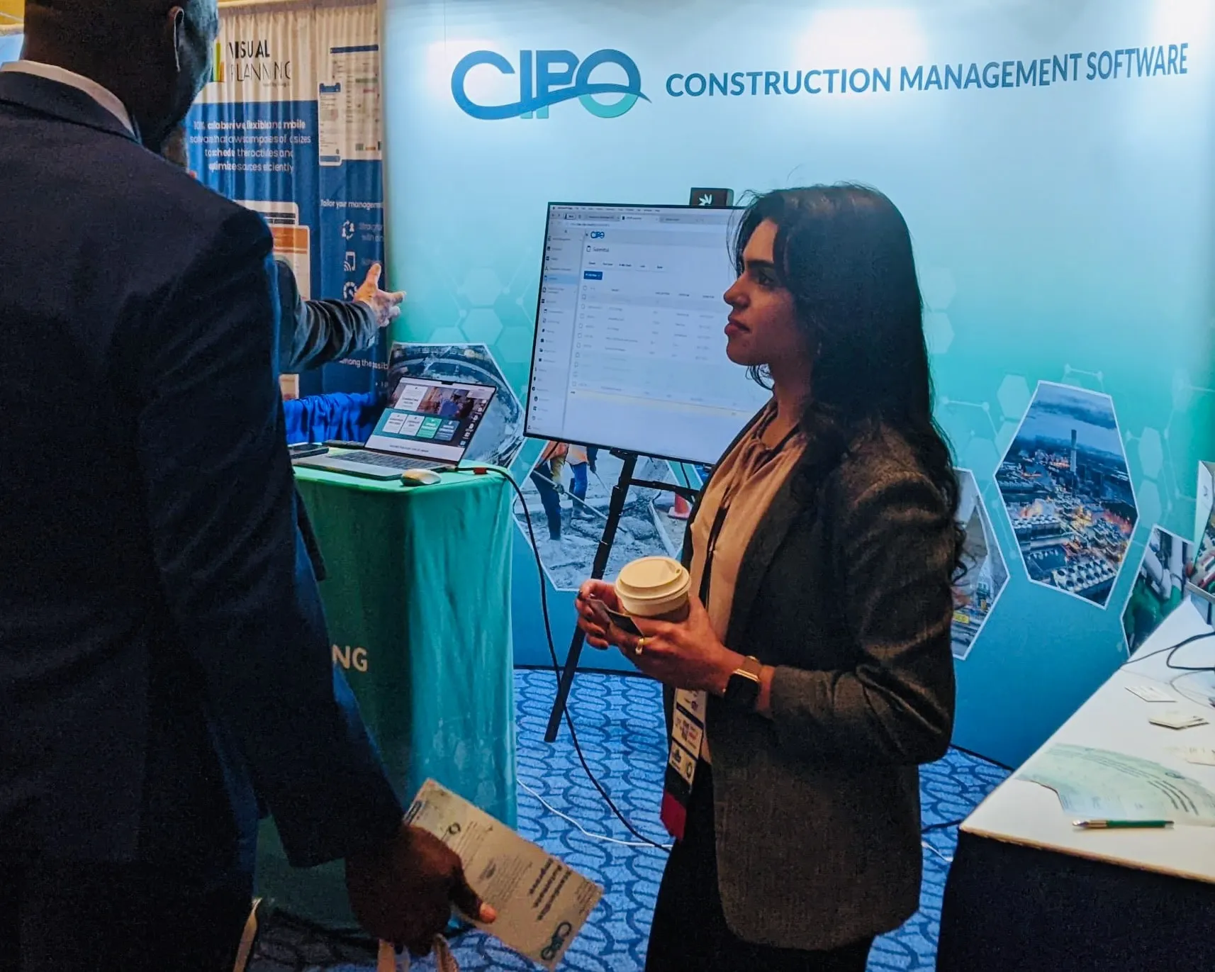 Two people discussing at a trade show booth for CIPO Construction Management Software, with a screen displaying the platform interface.