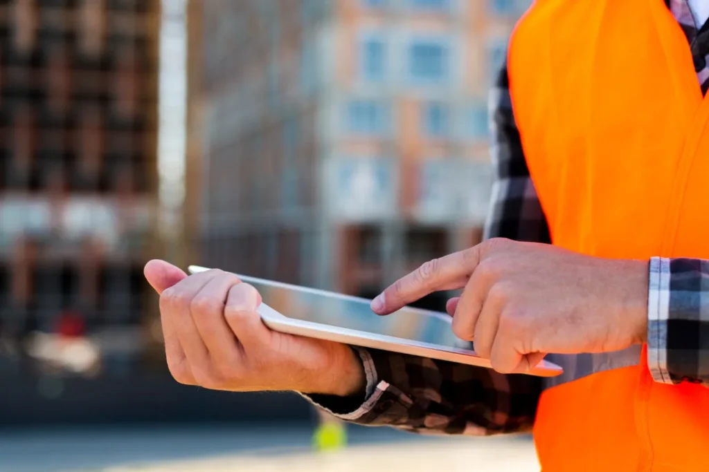 Close-up of a construction worker using a tablet on-site, with a blurred building in the background.