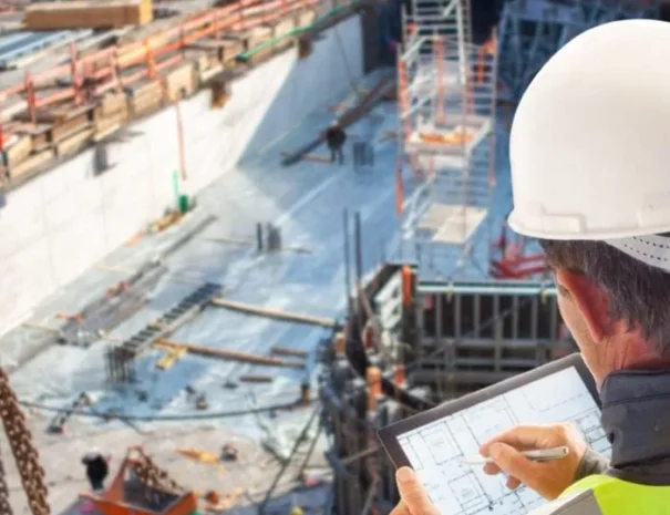 Construction engineer with hard hat and safety vest reviewing architectural plans on a tablet