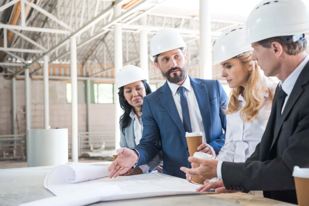 Group of government contractors in formal wear talking while reviewing floor plans for a construction site