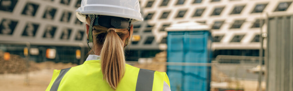 Back view of female construction worker in protective helmet against on construction background
