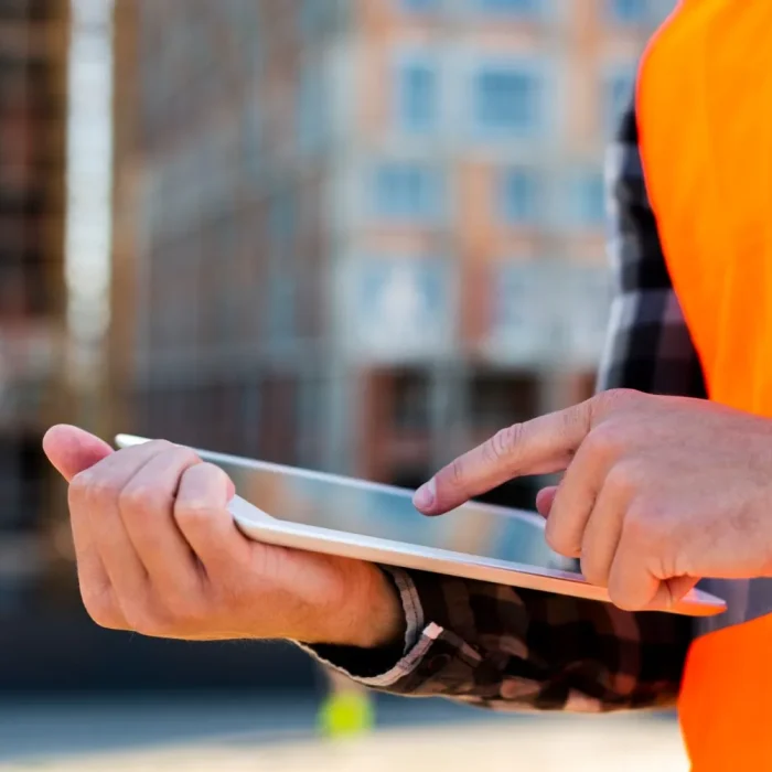 Close-up of a construction worker using a tablet on-site, with a blurred building in the background.