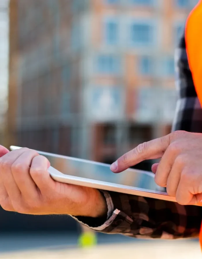 Close-up of a construction worker using a tablet on-site, with a blurred building in the background.